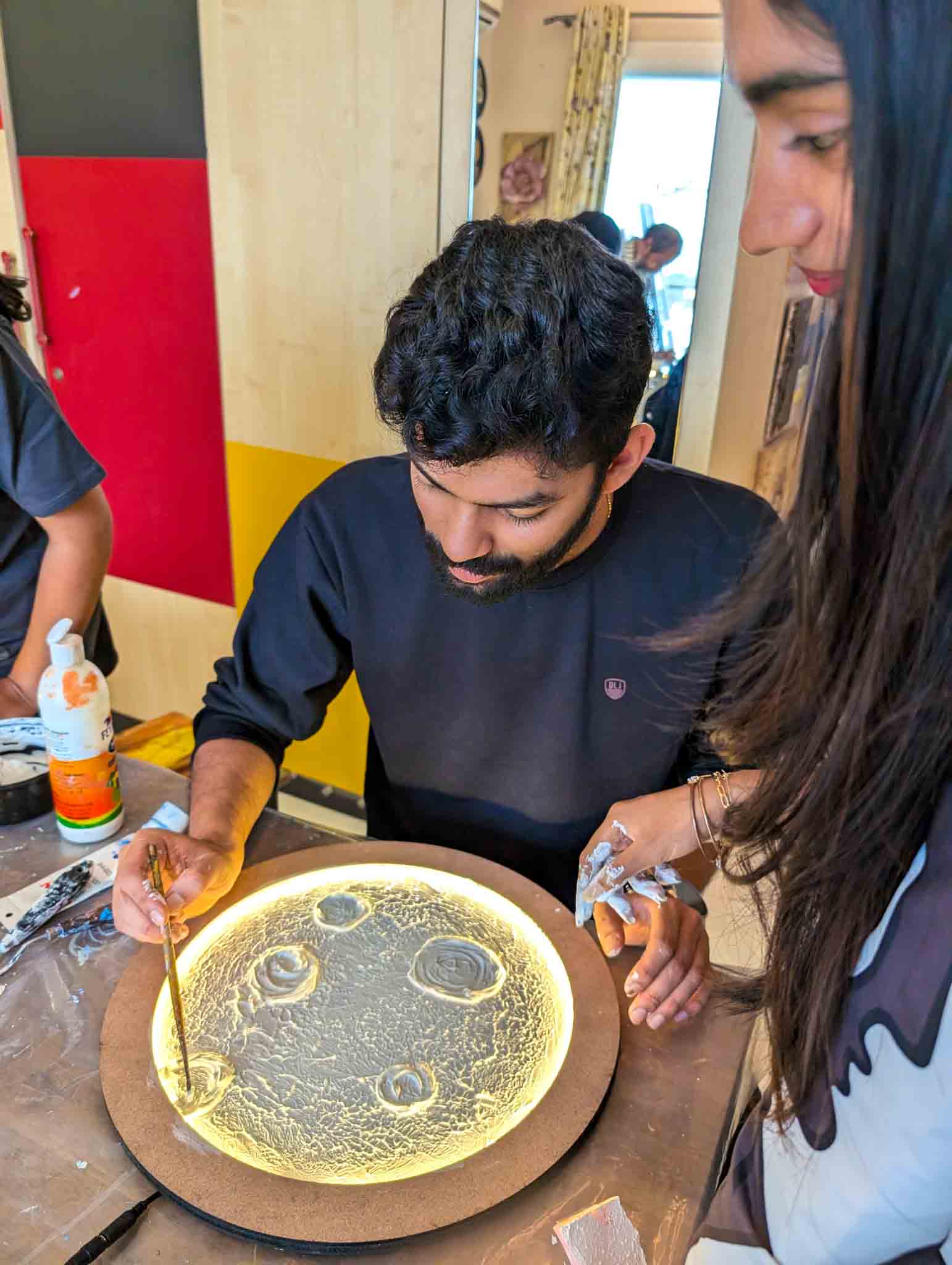 Man painting detailed surface design on glowing moon lamp as woman watches